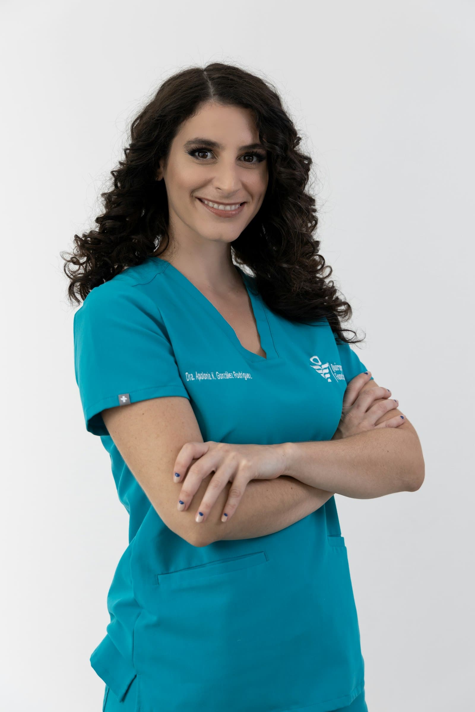 A smiling dentist in teal scrubs with her arms crossed